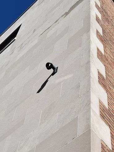 A modern building corner with a light fixture casting a shadow on the textured white wall.