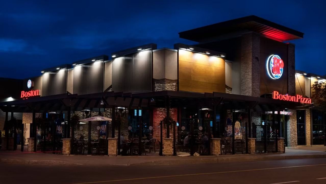 Boston Pizza restaurant at dusk, lit exterior, red logo, tables with customers.
