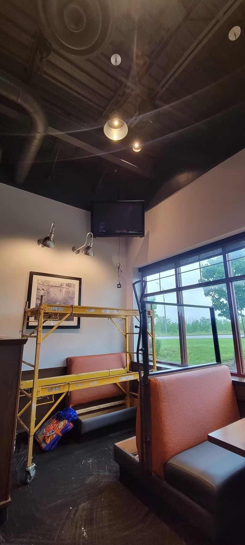 Interior of a restaurant with a black ceiling, booth seating, and a TV mounted on the wall.