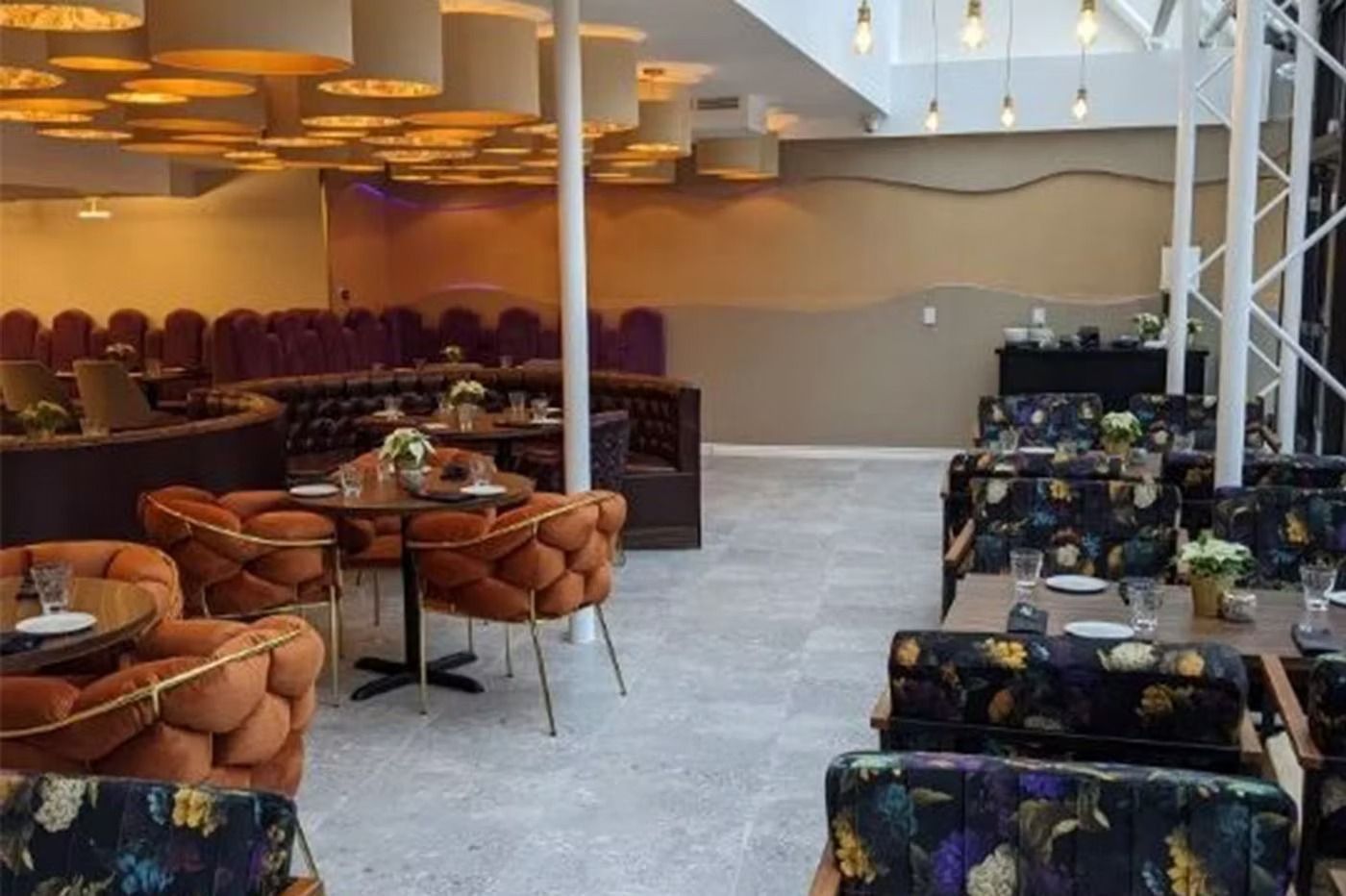 Restaurant interior with various seating, including orange and floral patterned upholstery. Beige and brown tones.