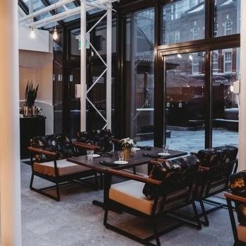 Restaurant interior: table set with dark leather chairs. Large windows overlook an outdoor area.