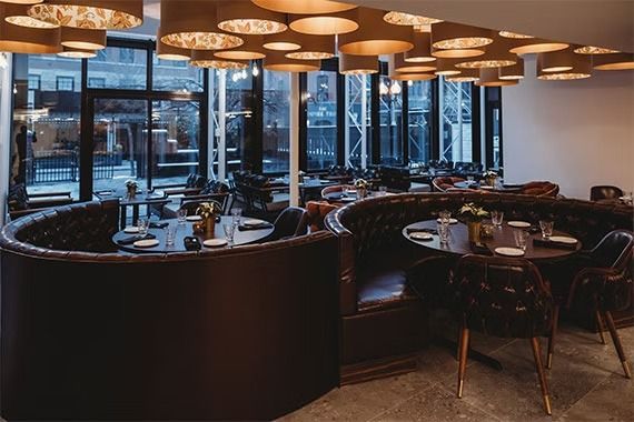 Restaurant interior: dark brown booths, tables set for dining, modern light fixtures.