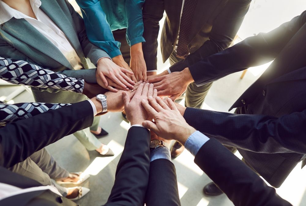 Team of diverse people join hands in a circle, symbolizing unity and collaboration.