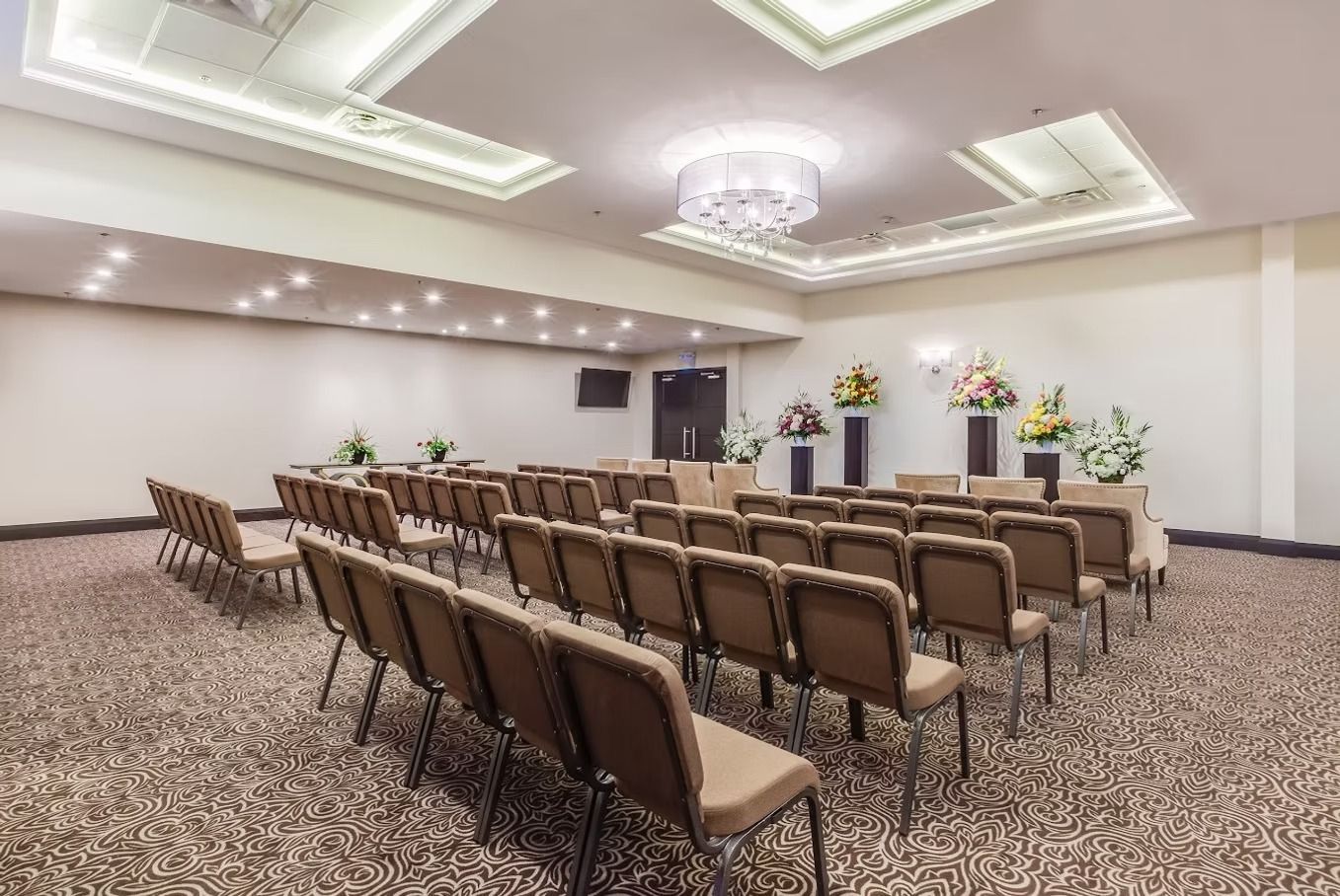Rows of chairs face a stage with flower arrangements in a beige room.