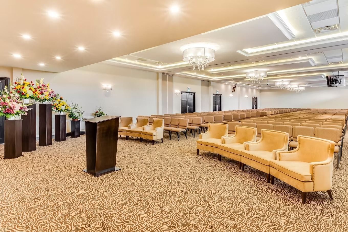 Empty event hall with seating, podium, flowers. Beige and white interior.