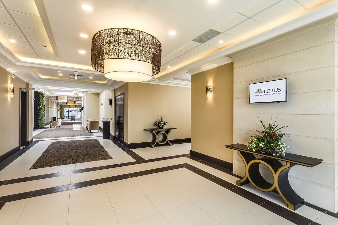Hotel lobby with patterned tile floor, light walls, decorative tables, and a hanging light fixture.