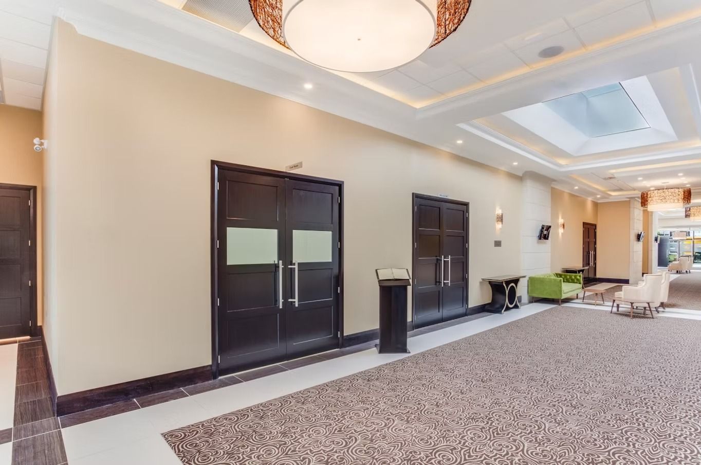 Hallway with dark doors, light walls, and carpet, leading to seating area with green chair.