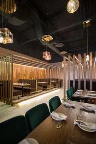 Restaurant interior with booths and tables. Emerald green chairs, wooden tables, and decorative lighting.