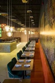 Restaurant interior with long tables, green velvet chairs, and hanging globe lights.