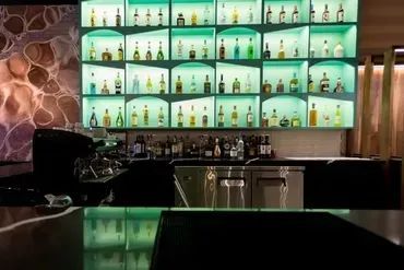 Bar interior with glowing green shelves displaying liquor bottles.
