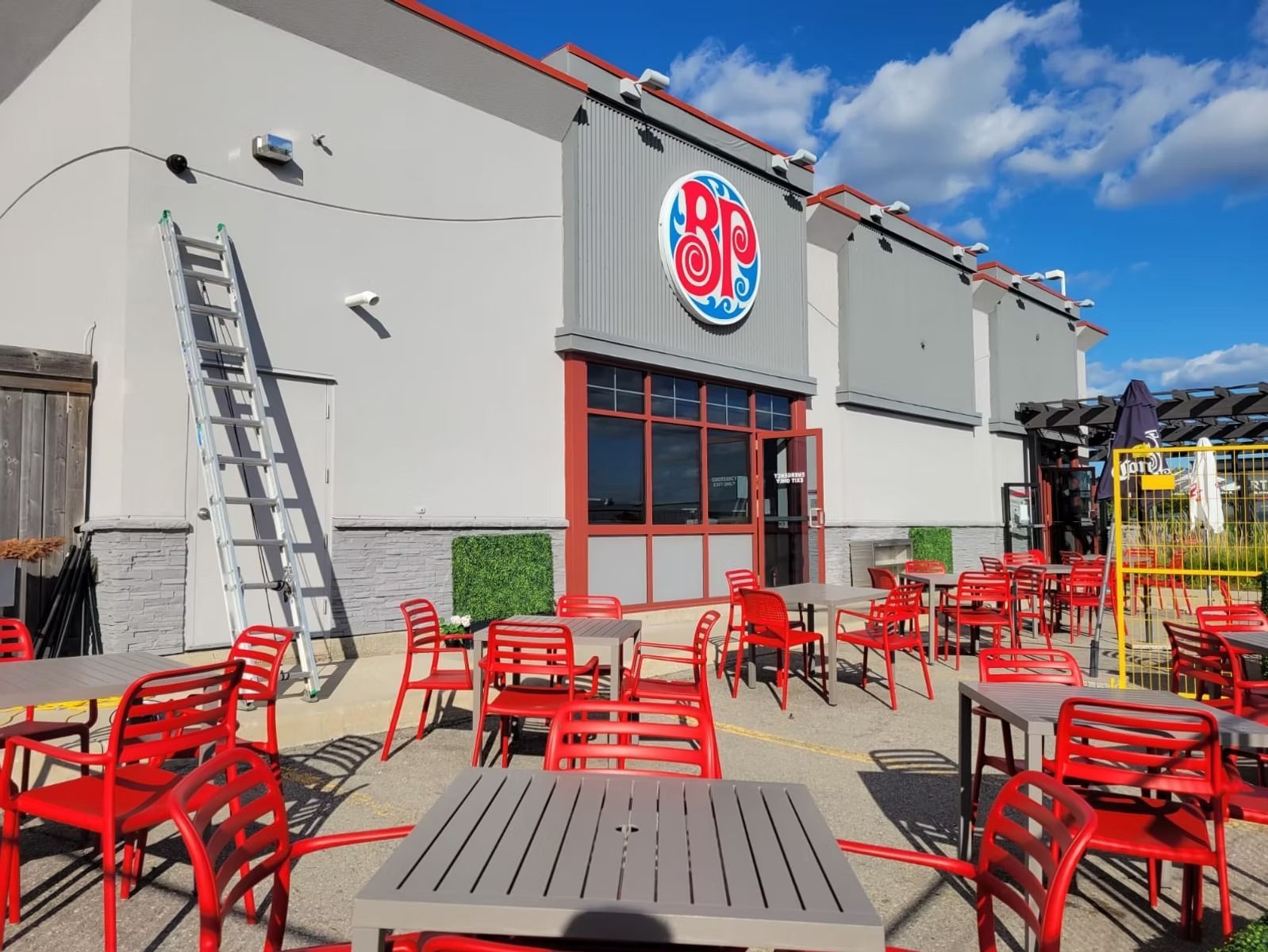 Outdoor patio with red chairs and tables in front of a restaurant with a blue logo.