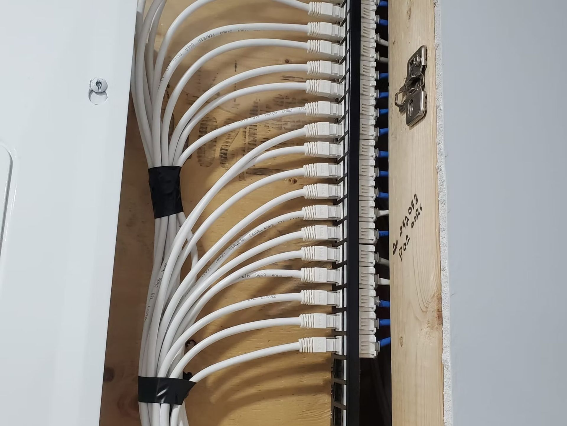 Network patch panel with white Ethernet cables installed on a wooden frame, and a black panel.