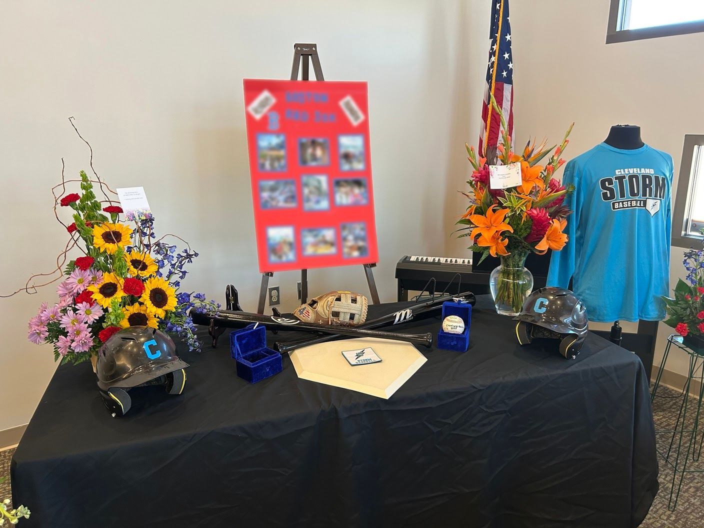 Team jersey, glove, and bats arranged in honor of a young baseball player, alongside a baseball signed by teammates.
