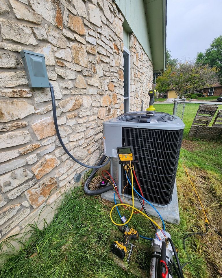 HVAC unit being serviced outdoors, hoses connected, near a stone wall and electrical box.