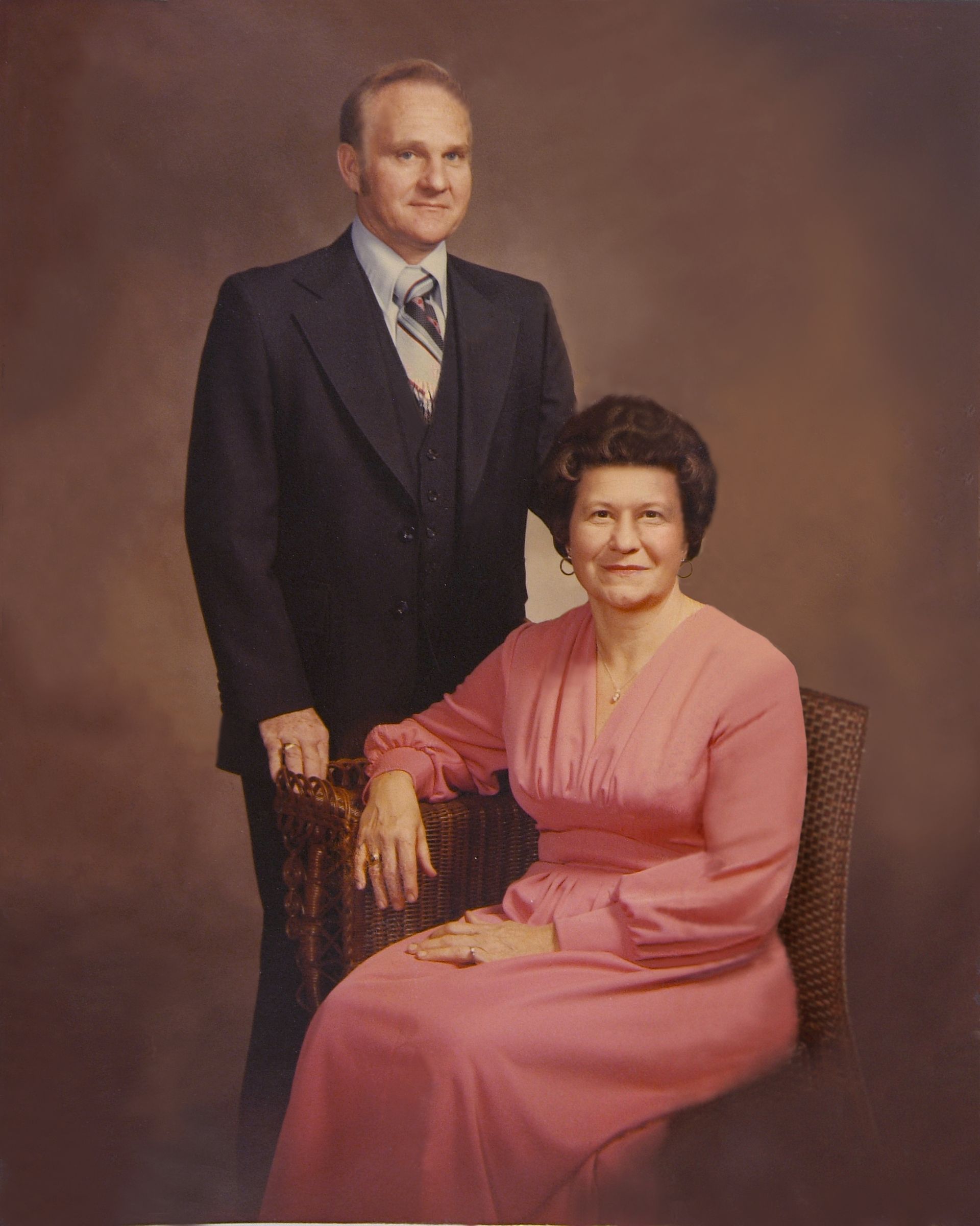 A man in a suit and tie stands next to a woman in a pink dress