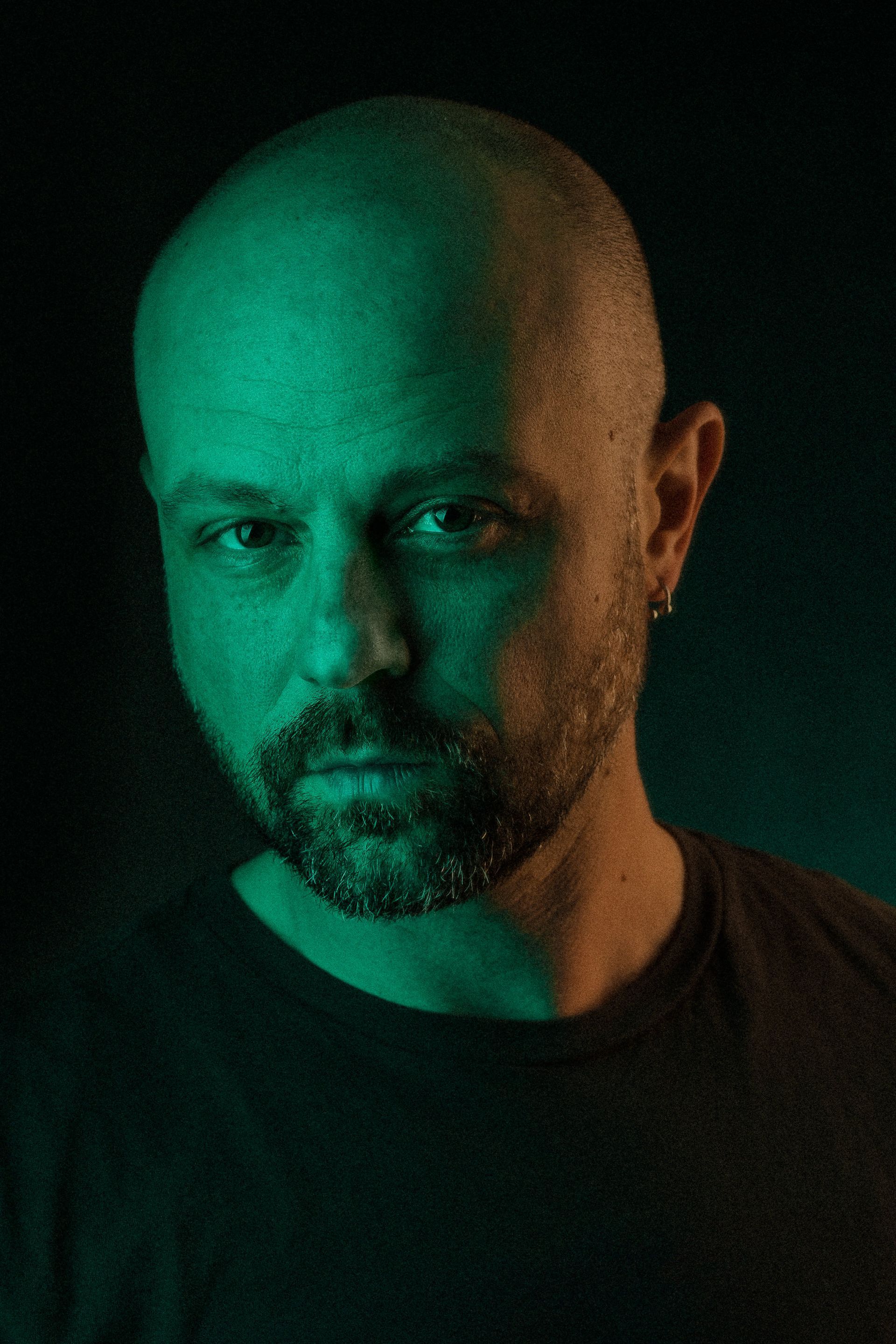 A bald man with a beard is looking at the camera in a dark room.