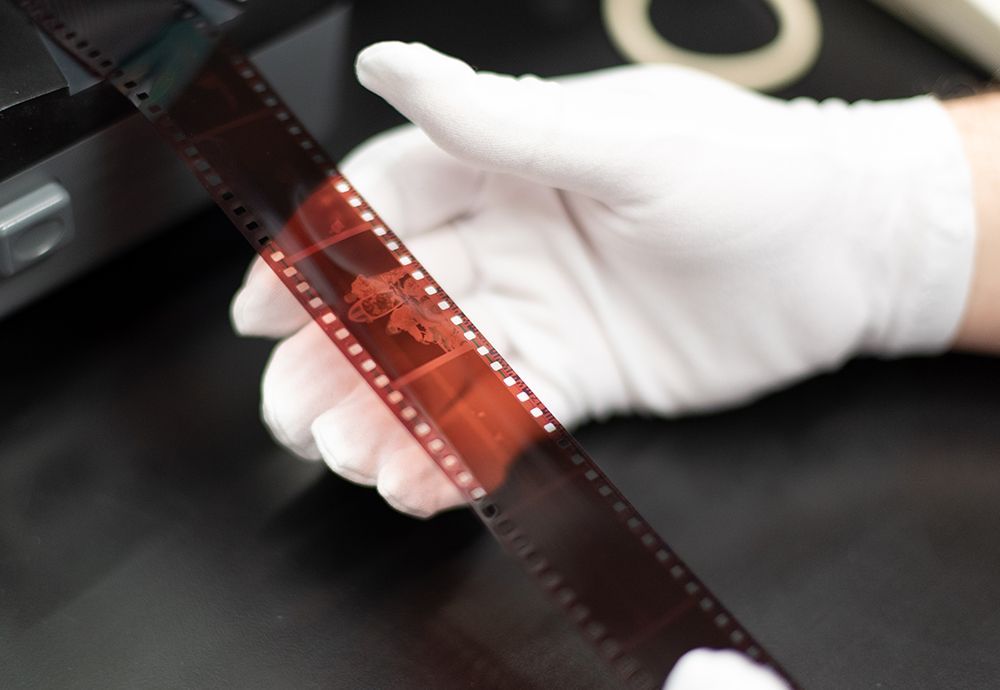 A person wearing white gloves is holding a roll of film