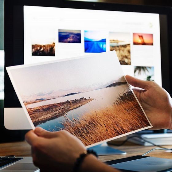 A person is holding a picture in front of a computer screen