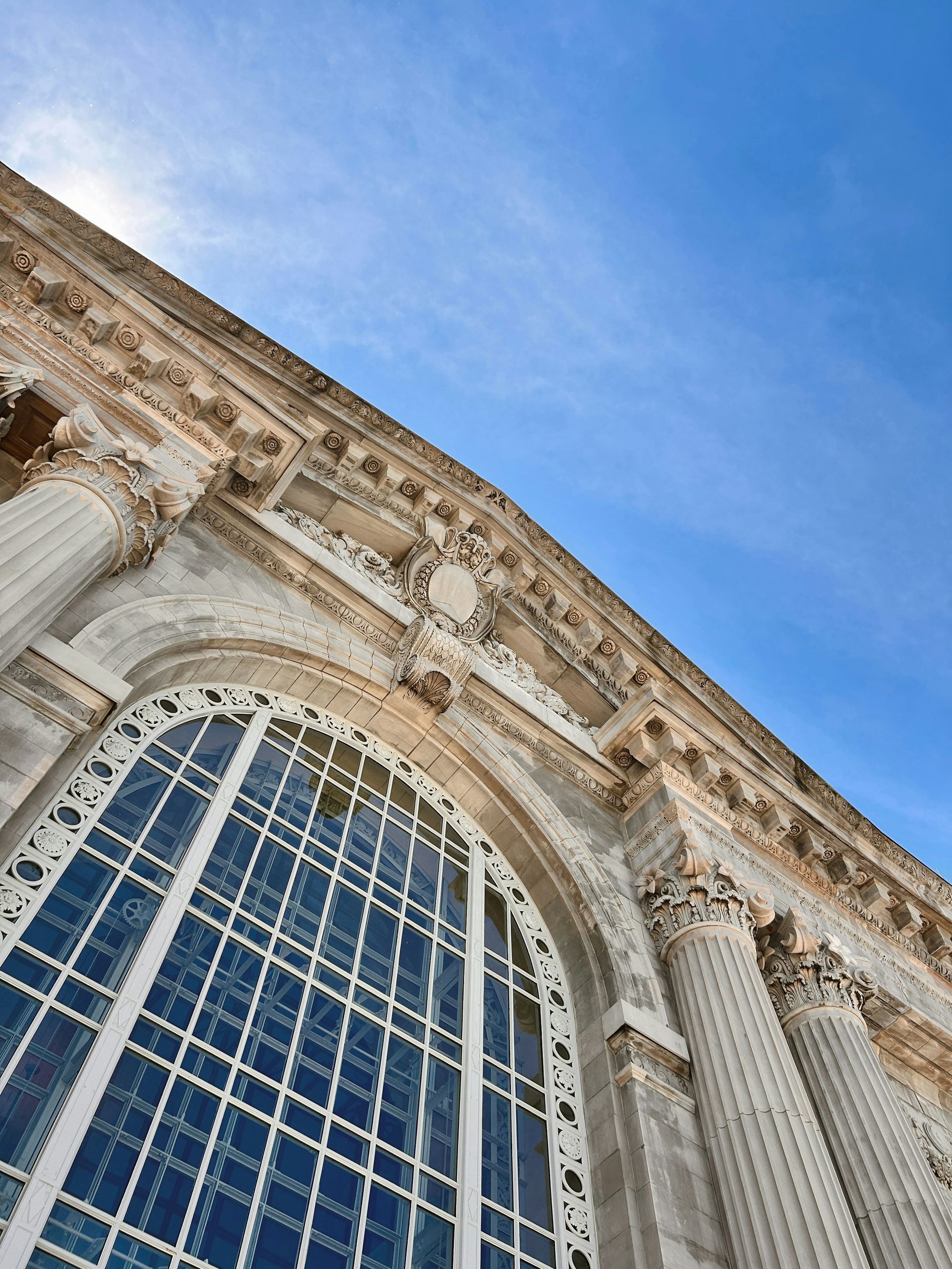 Ornate stone building with large arched window and columns against a blue sky.