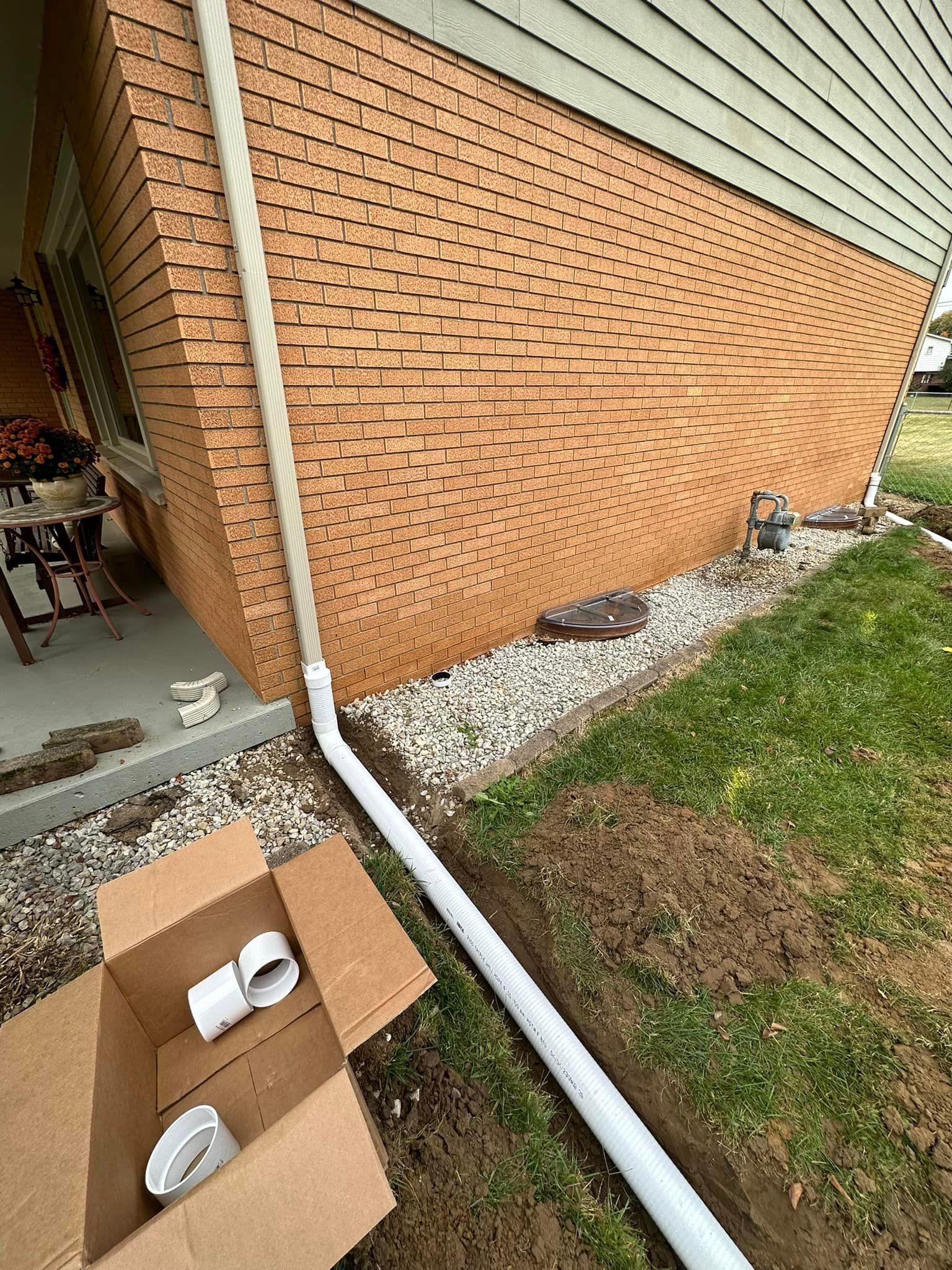 A drain pipe is being installed on the side of a brick house.
