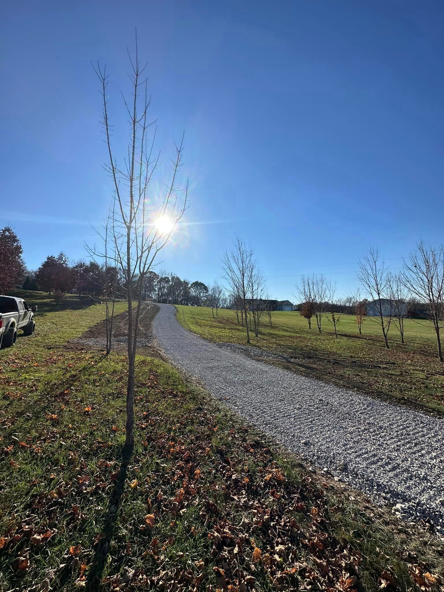 a gravel path going through a grassy field with trees on both sides .