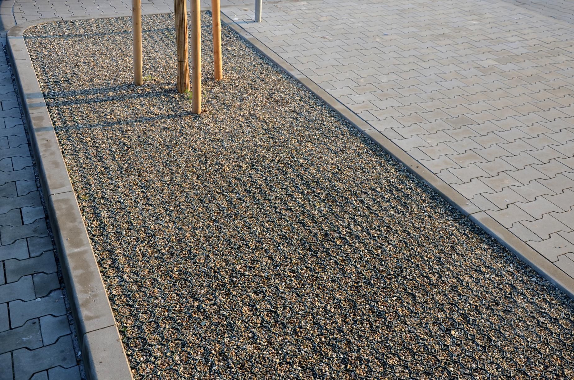 a gravel path along a sidewalk with trees in the background