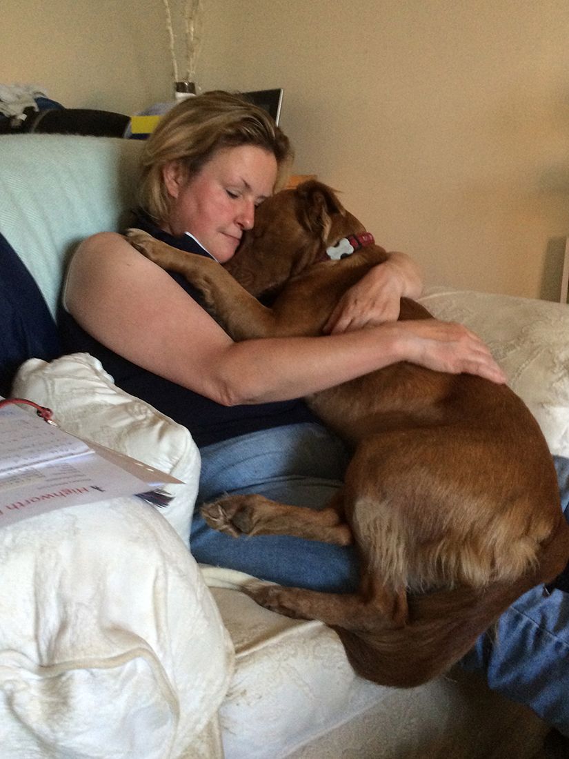 Woman cuddling a brown dog on a beige couch in a cozy living room