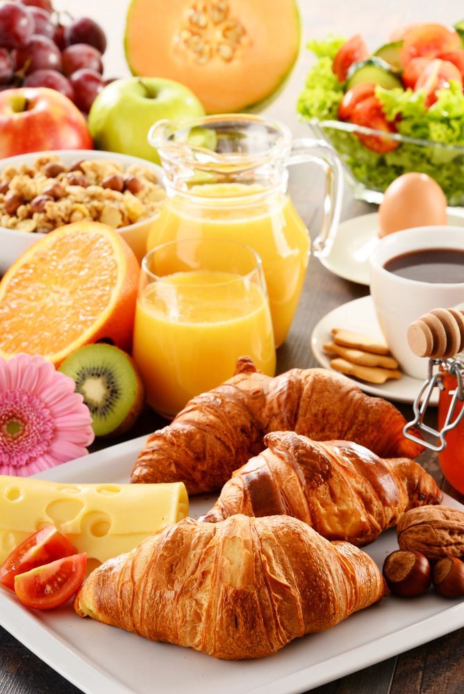 Colazione abbondante: croissant, frutta, succo di frutta, cereali, caffè e formaggio su un tavolo.