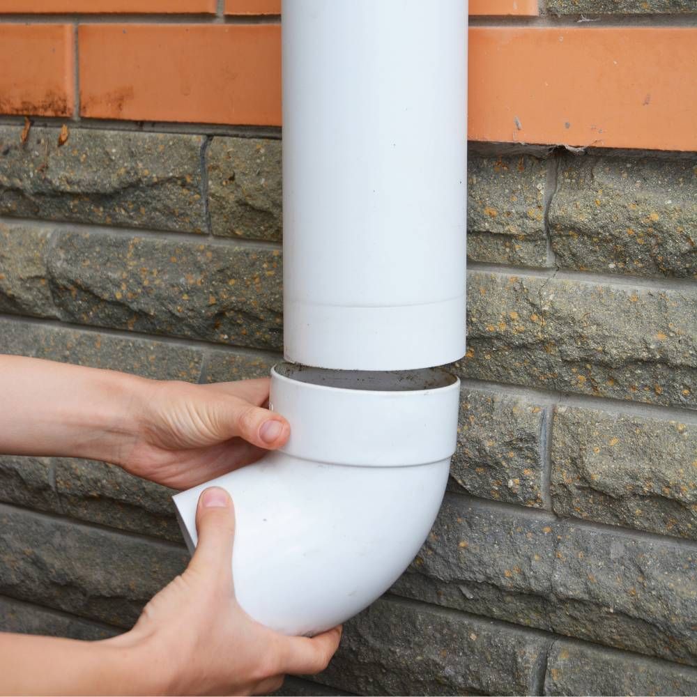 A person is holding a white pipe against a brick wall.