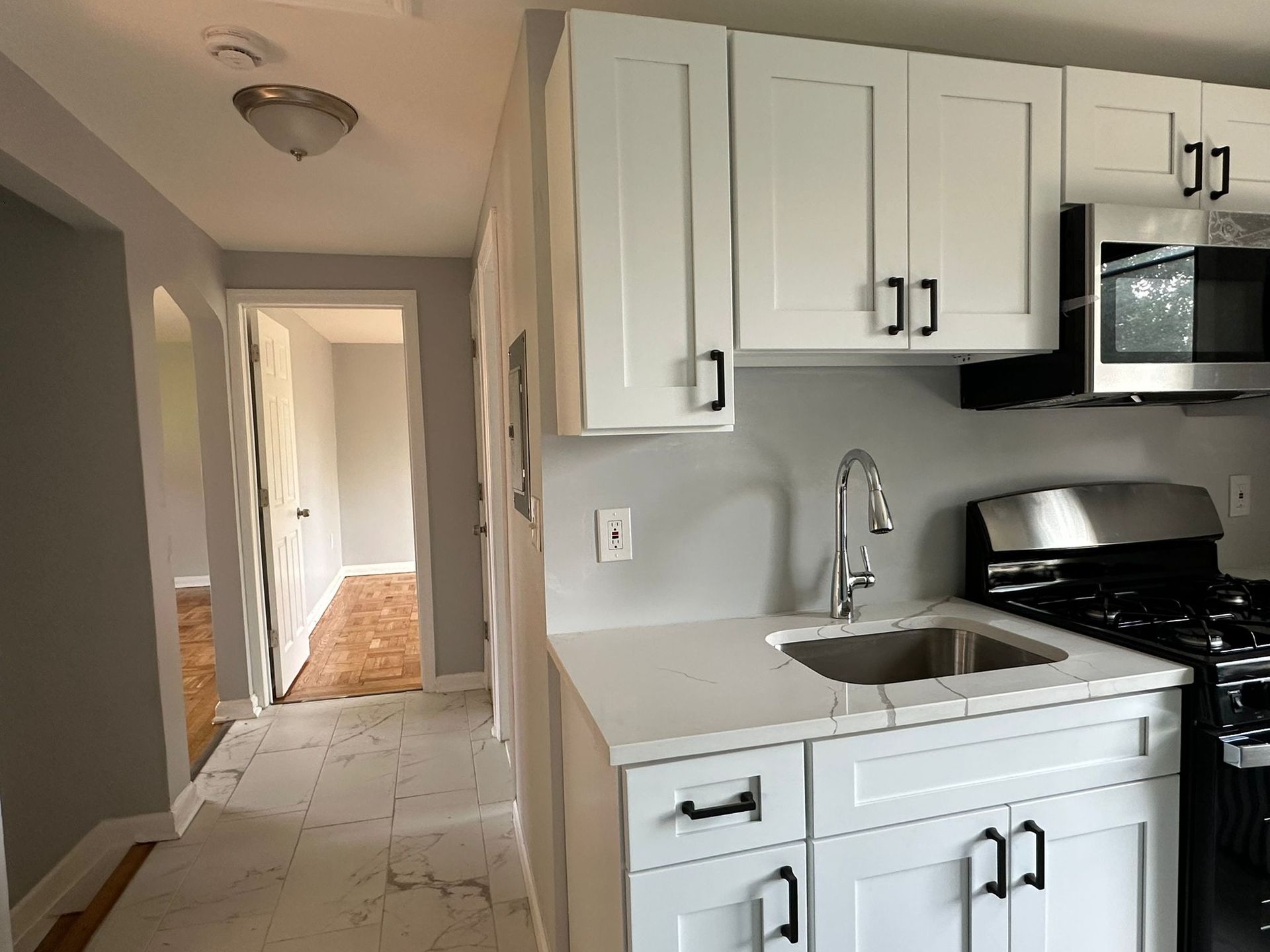 White kitchen cabinets with black hardware, sink, and gas range. Open doorway to another room.