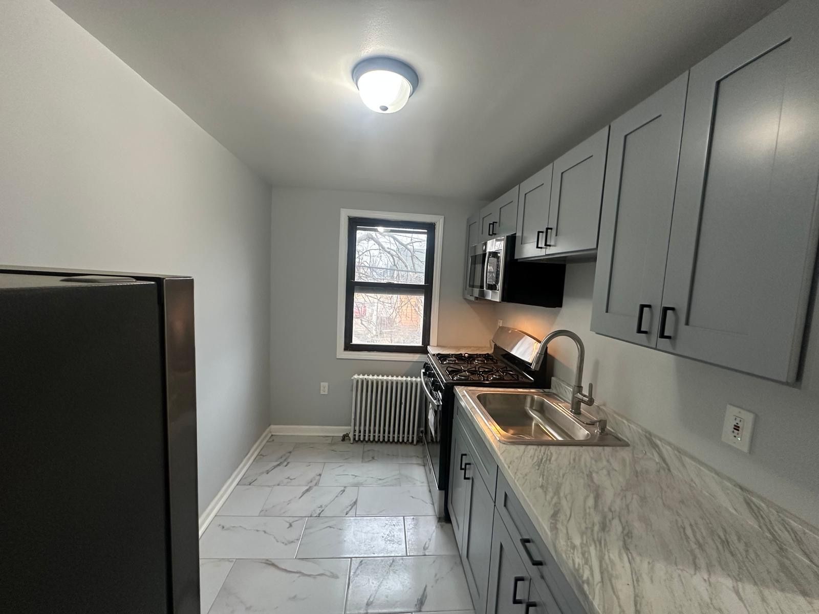 Gray kitchen with cabinets, sink, stove, window, and refrigerator.