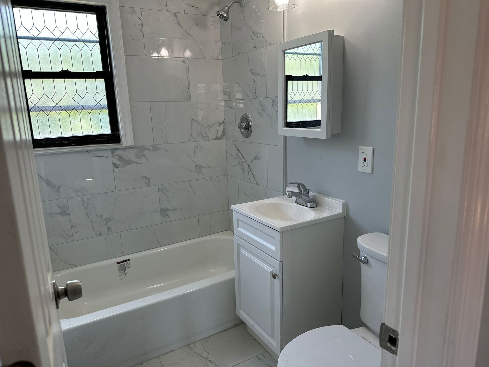 Bathroom with white marble tile, a white tub, vanity, and toilet.