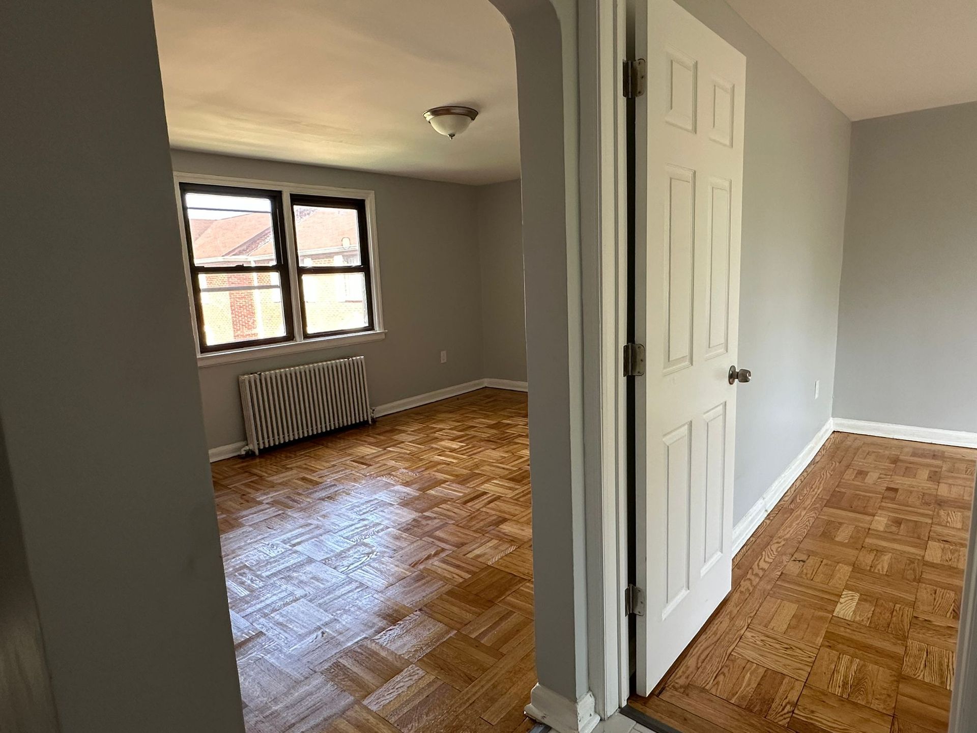 A doorway leads into a room with wood flooring and a window, with the walls painted gray.