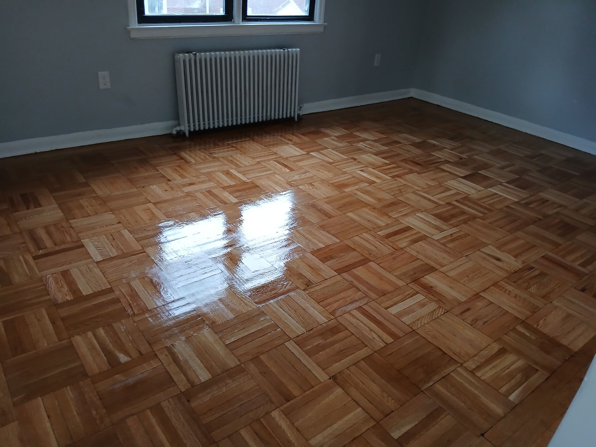Newly finished parquet wood floor in a room with a radiator and window.