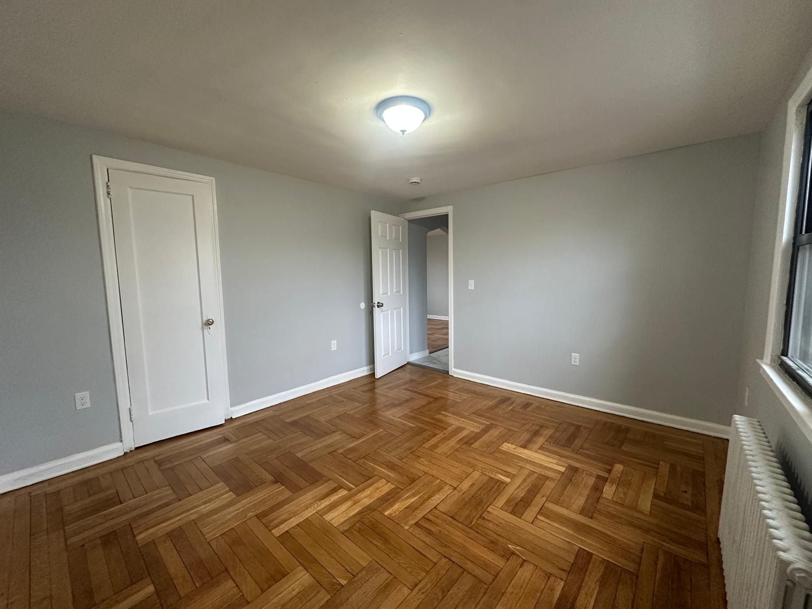 Empty bedroom with wooden floor, gray walls, two doors, and a window.