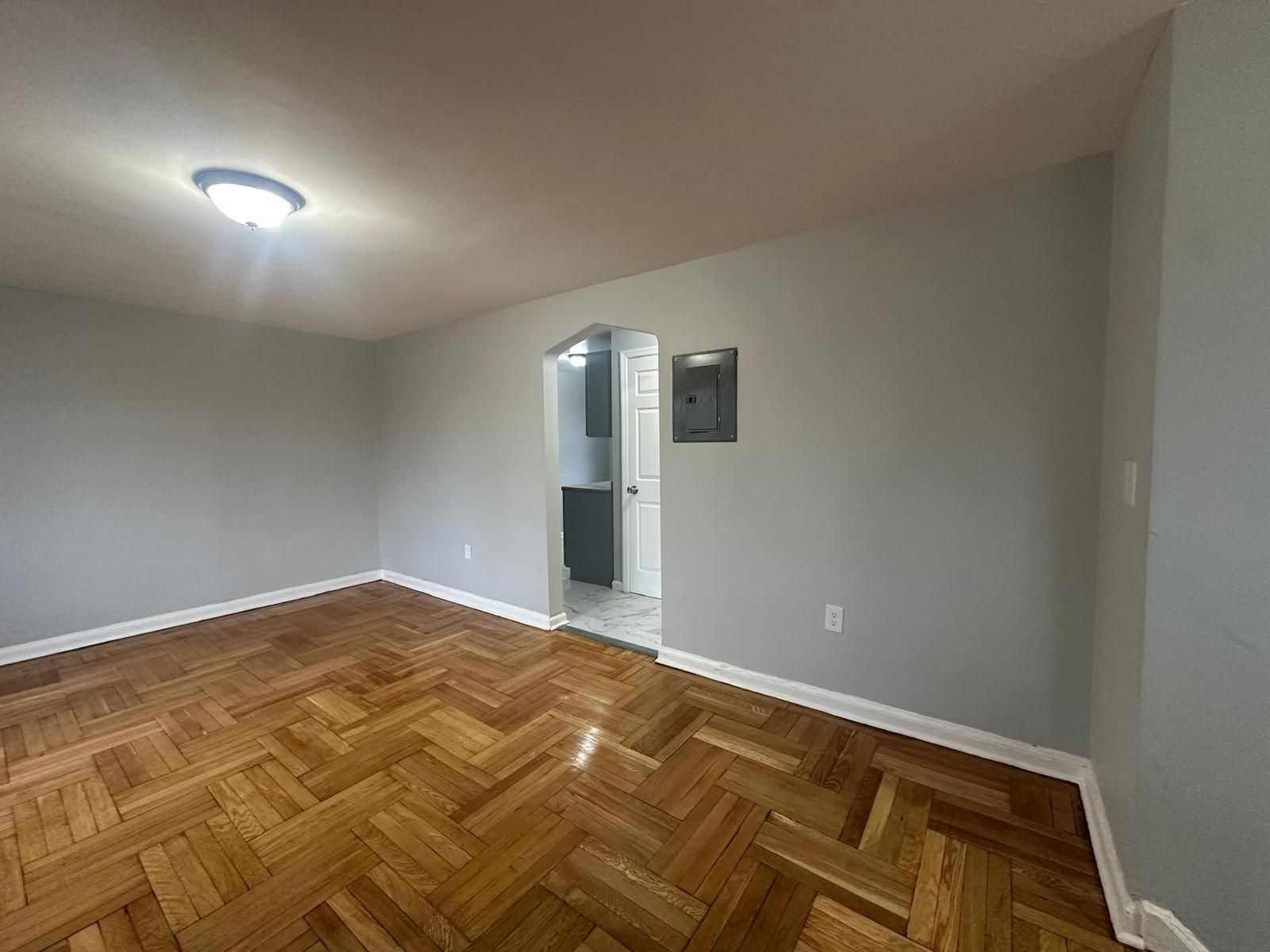 Empty room with hardwood floors, gray walls, and doorway to a bathroom.