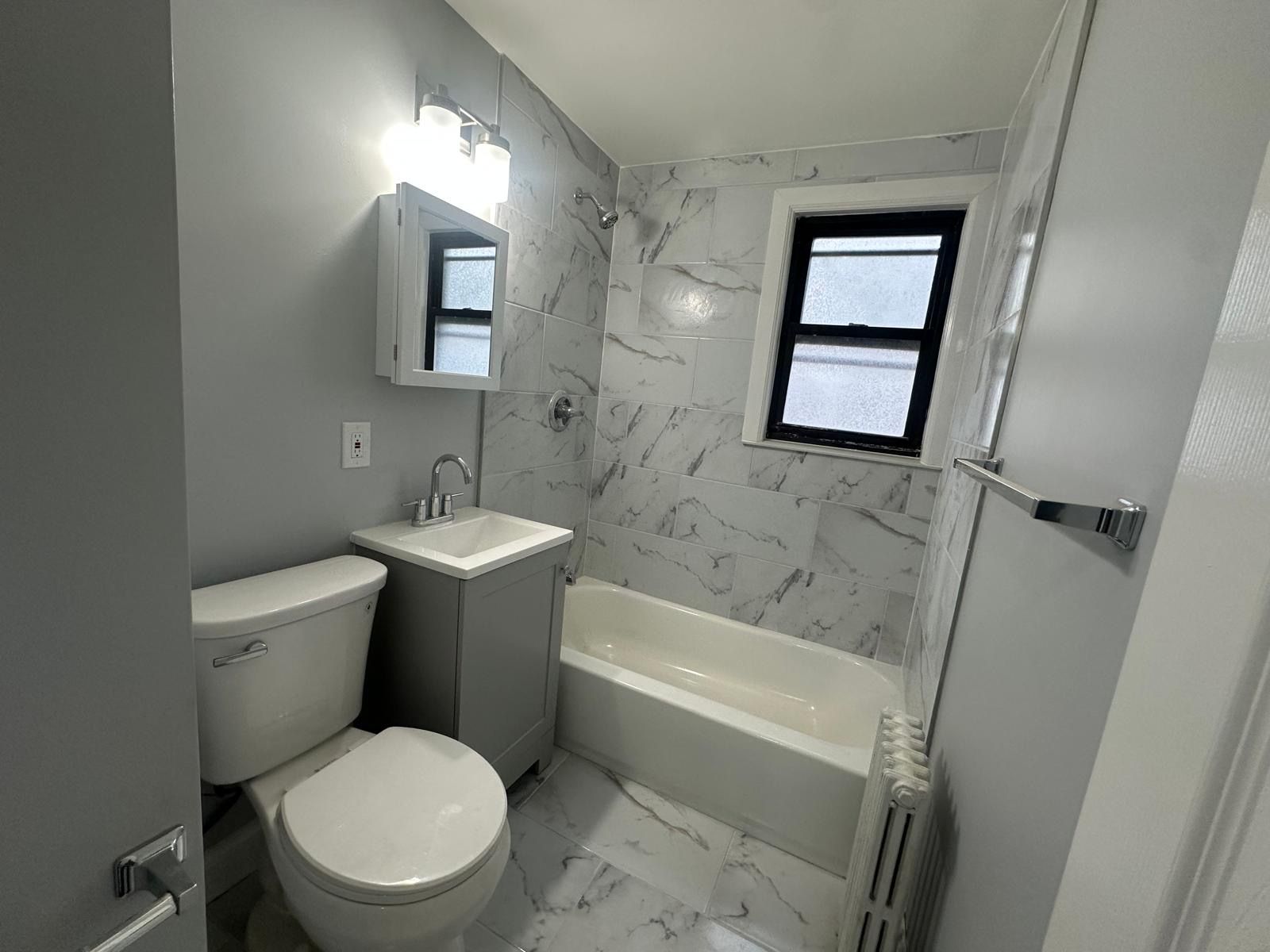 Bathroom with a white toilet, sink, tub, and marble tile walls.