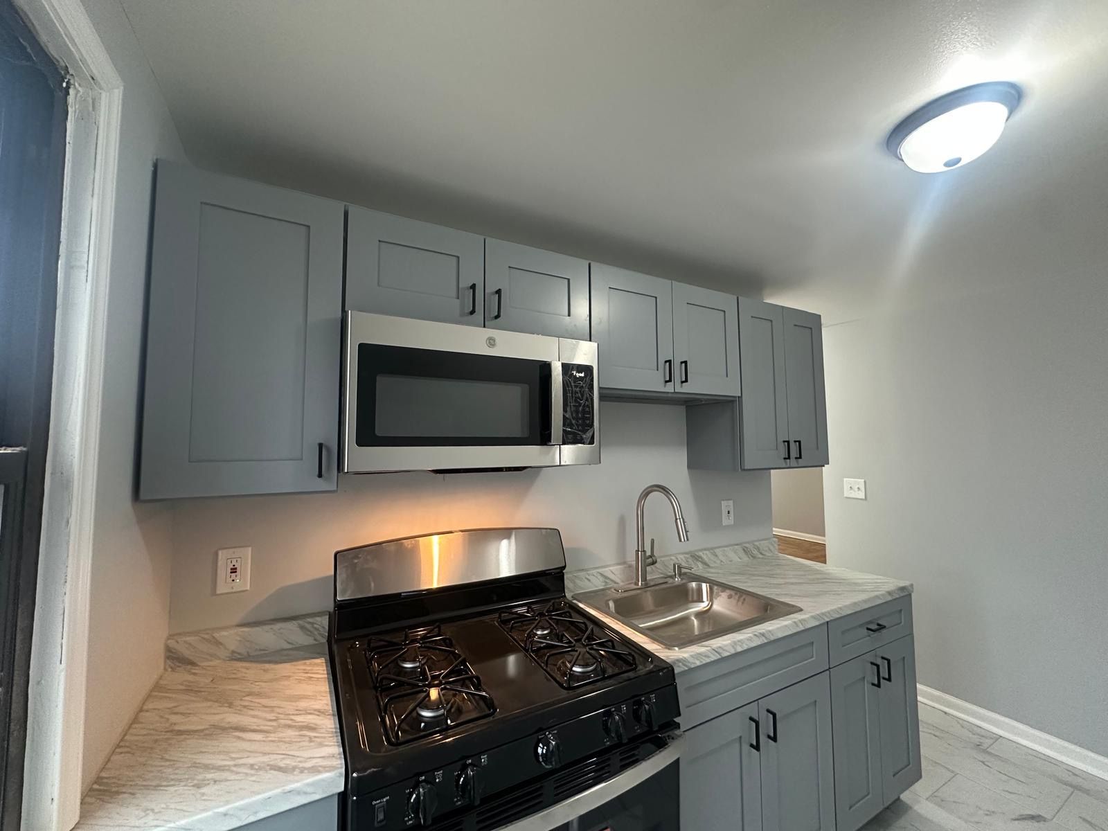 Grey kitchen cabinets with a stainless steel microwave, stove, and sink.