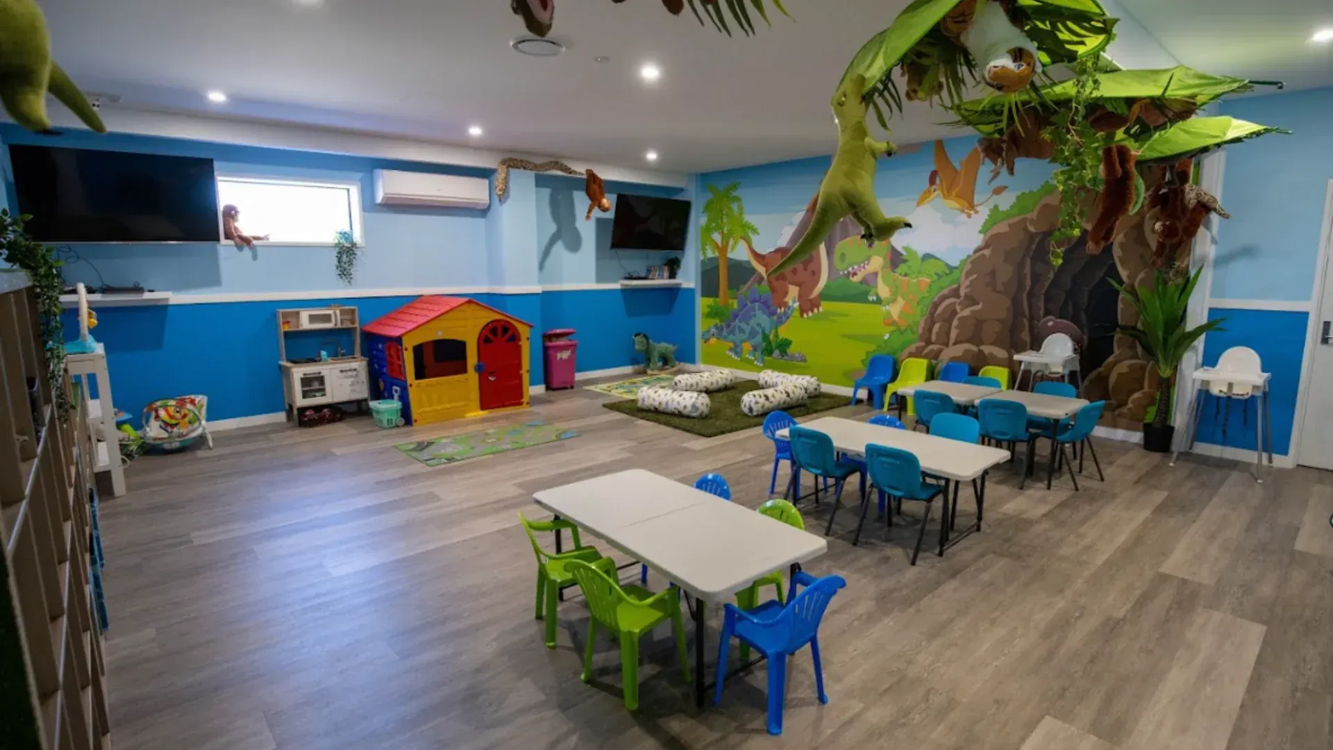 A large room with tables and chairs and a mural of dinosaurs on the wall.