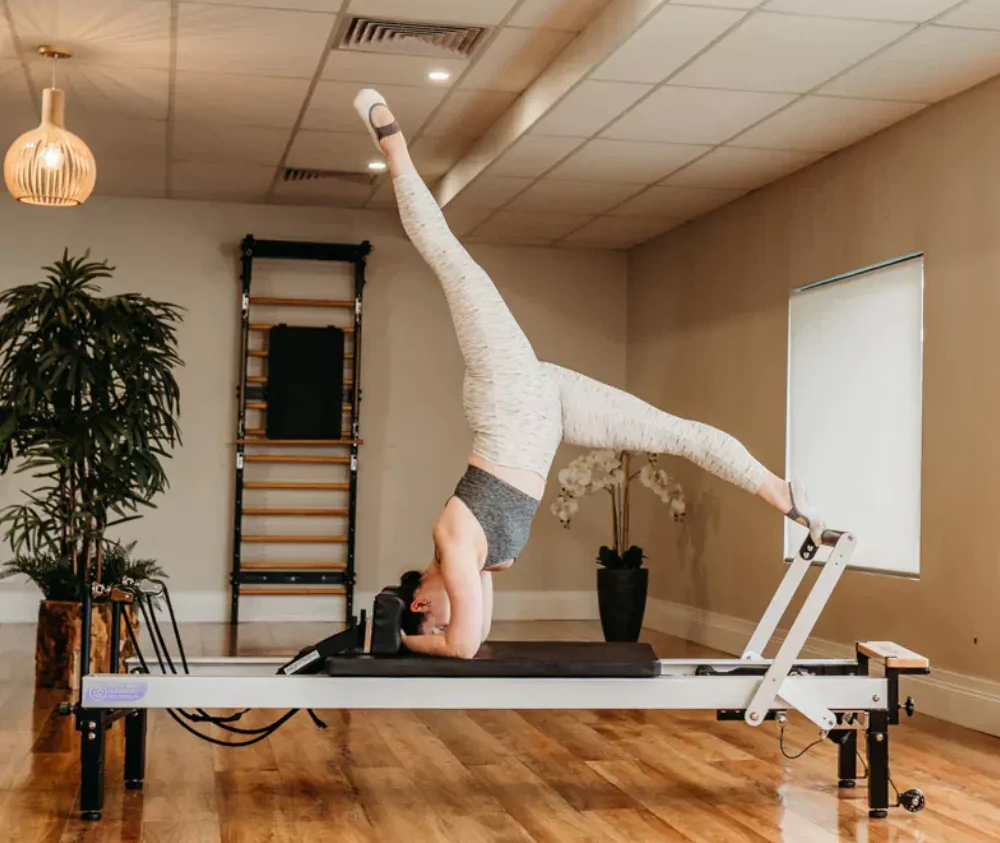 A woman is doing a handstand on a pilates machine.