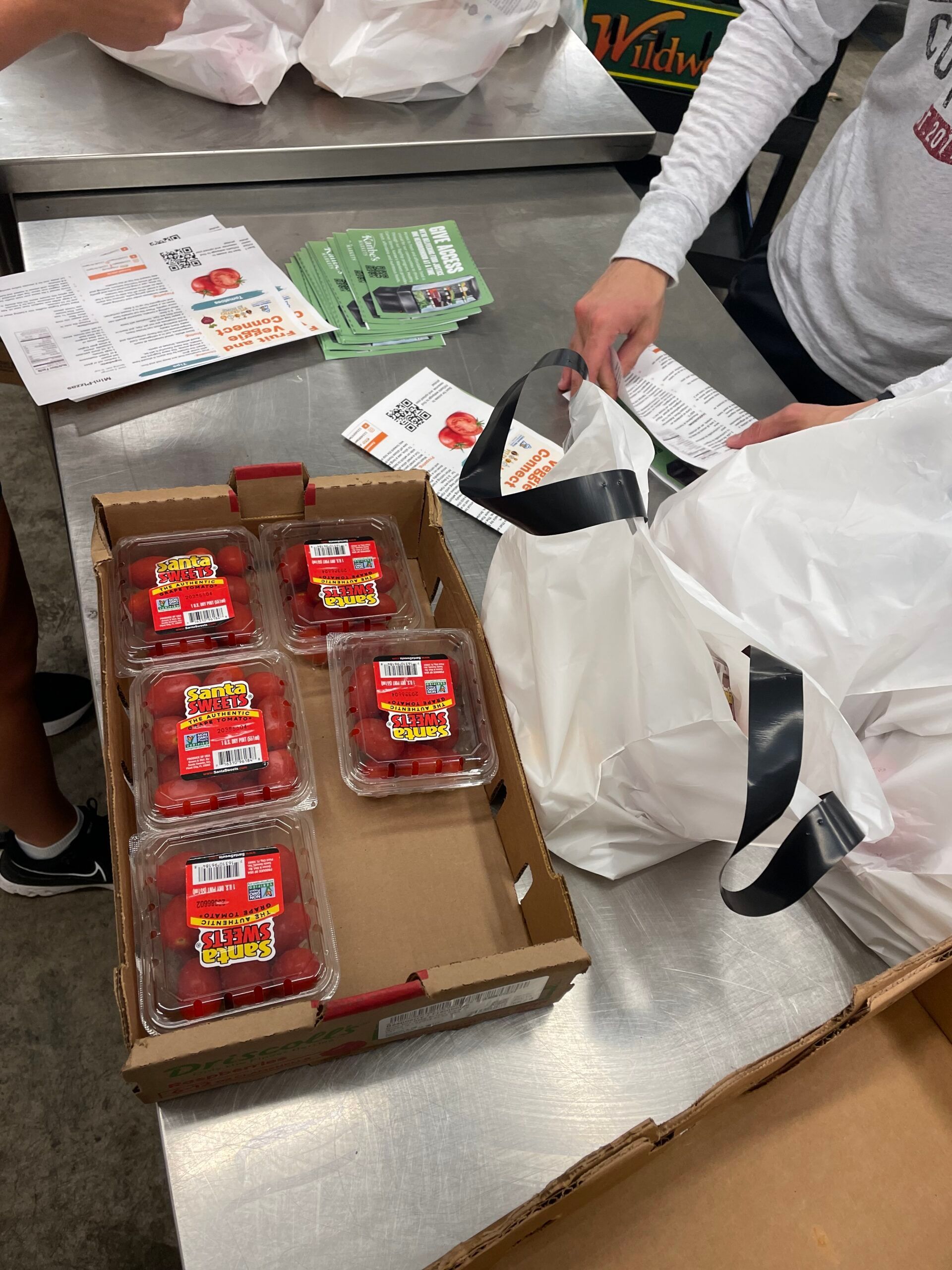 A box of plastic containers filled with strawberries sits on a metal table next to shopping bags and receipts.