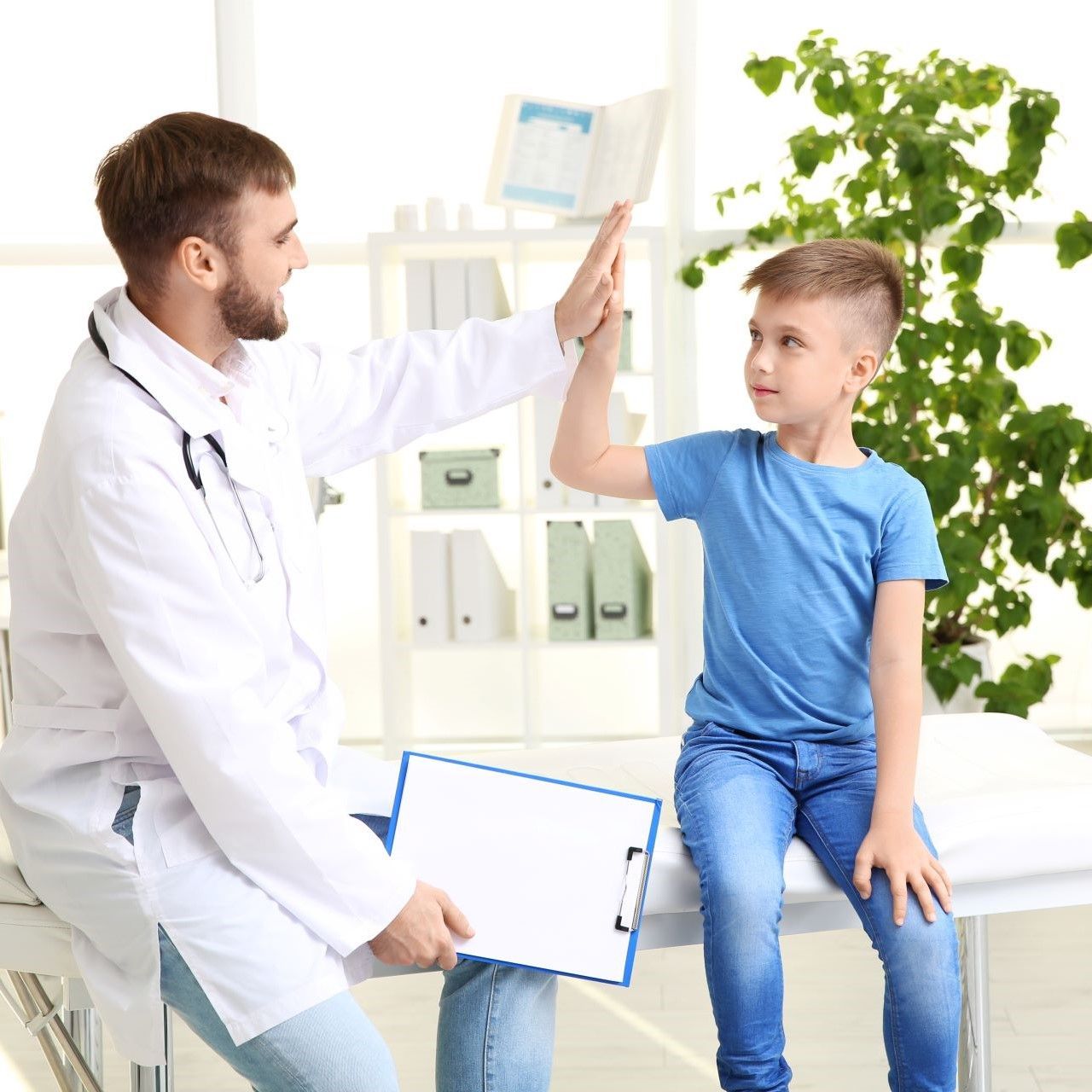 Doctor gives a high-five to a child in a medical office setting. The child sits on a medical bed.