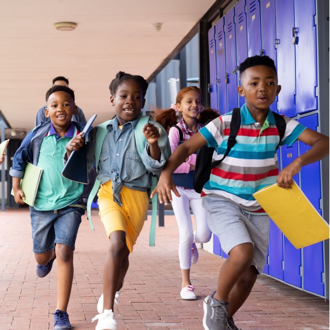Children run down a school hallway toward the camera, carrying backpacks and binders.