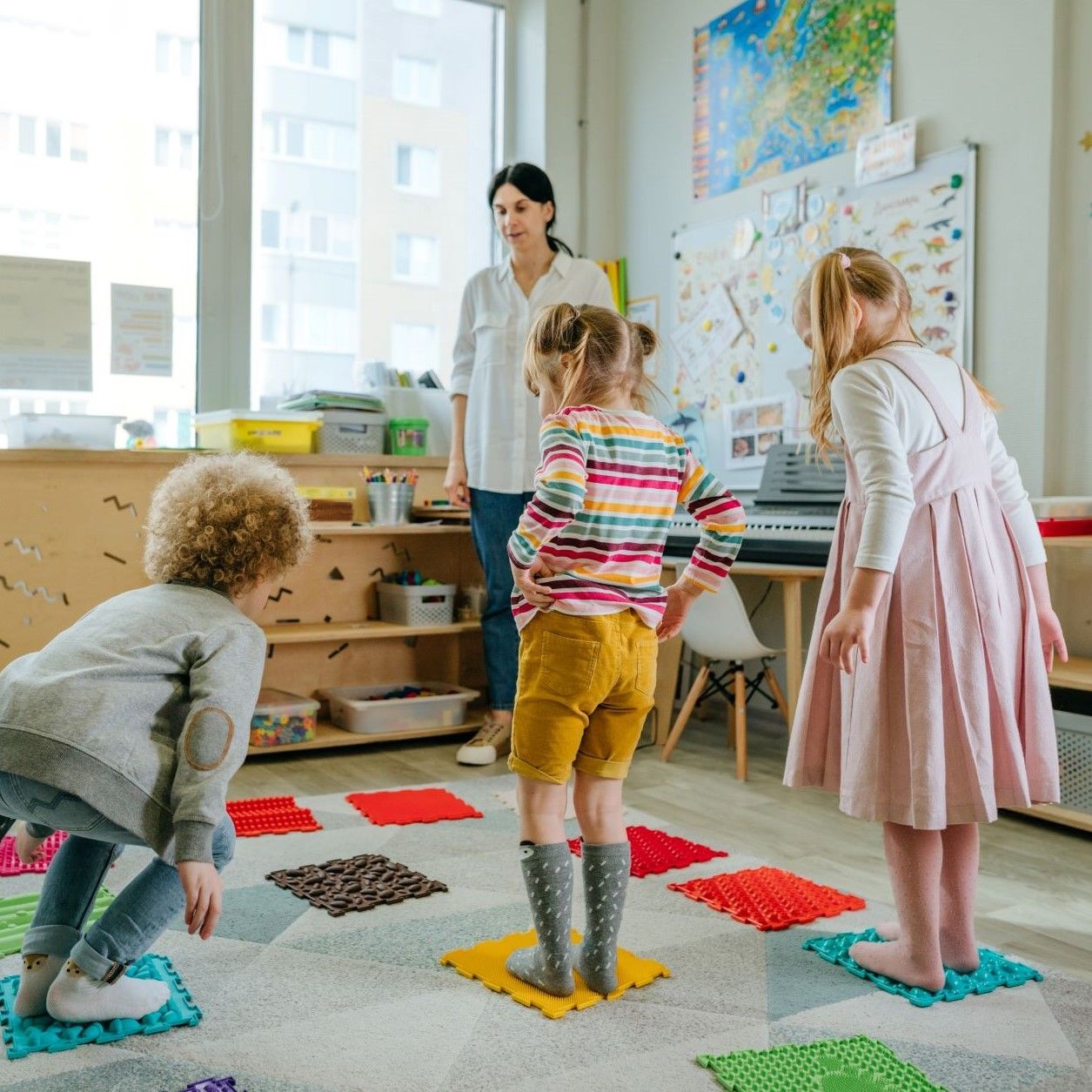 Children playing a game with textured floor tiles supervised by an instructor in a classroom.