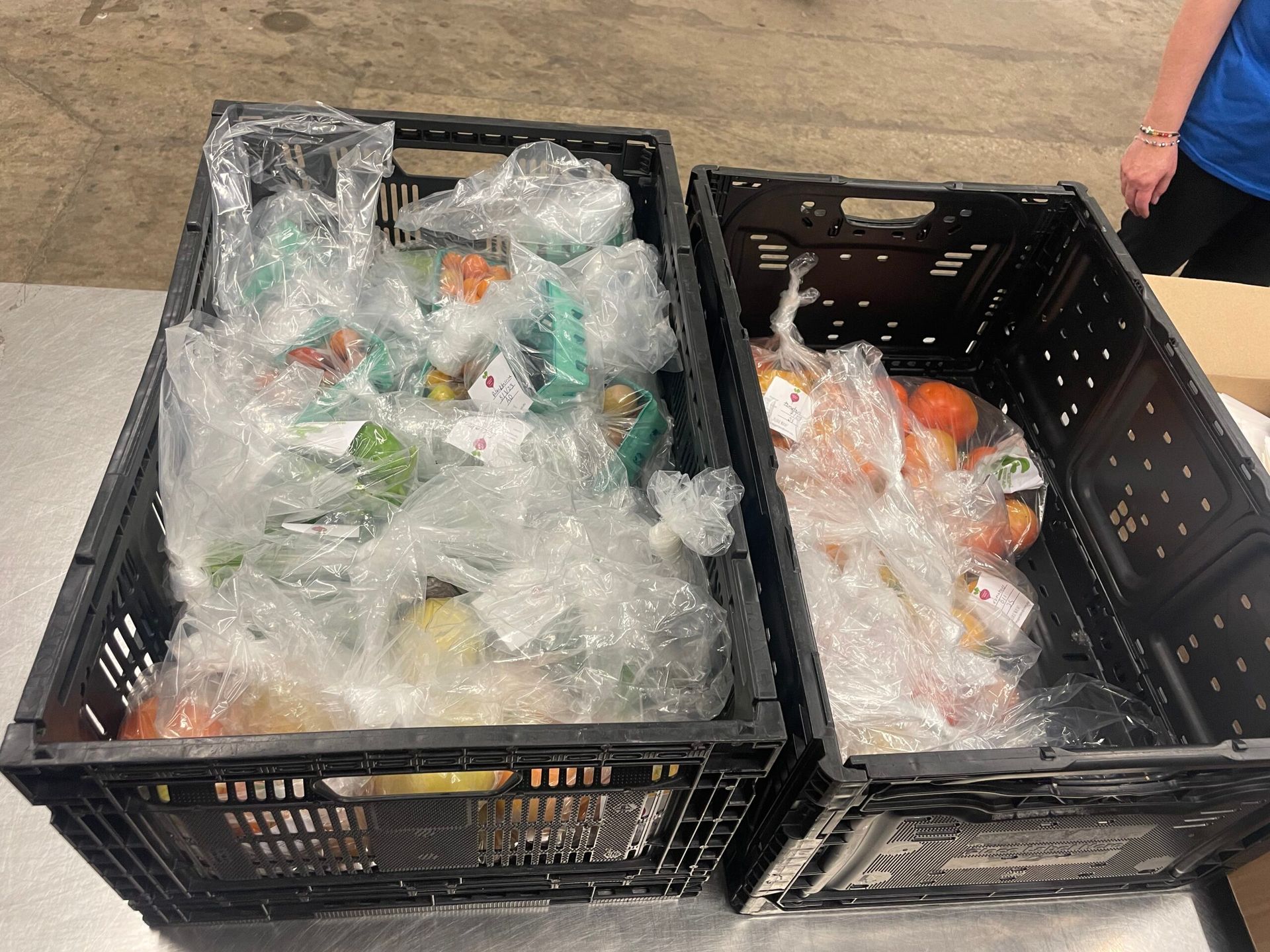 Two black plastic crates filled with assorted produce items individually packed in clear plastic bags.