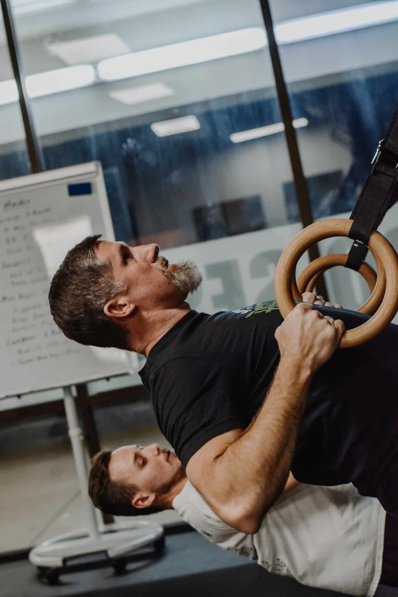 two men are doing exercises with gymnastic rings in a gym .