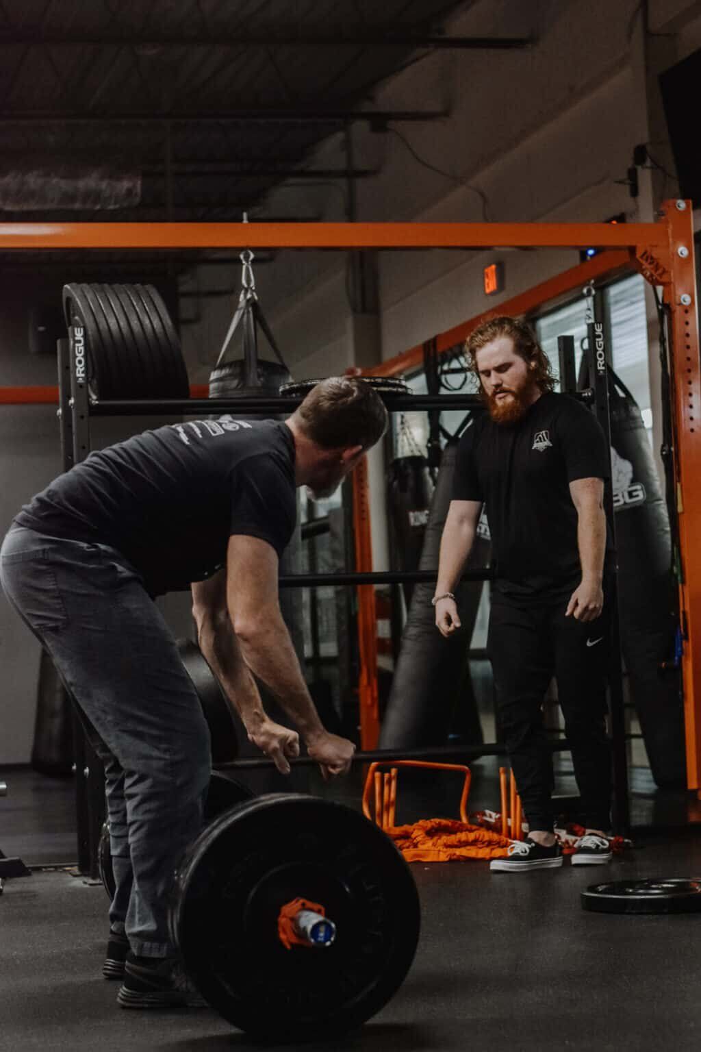 a man is lifting a barbell in a gym while another man watches .