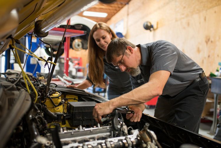 Ryan Family working on car engine, woman observing in auto repair shop.