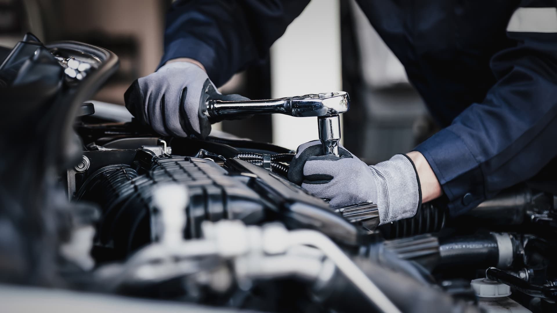 Mechanic in gloves using a wrench on a car engine.
