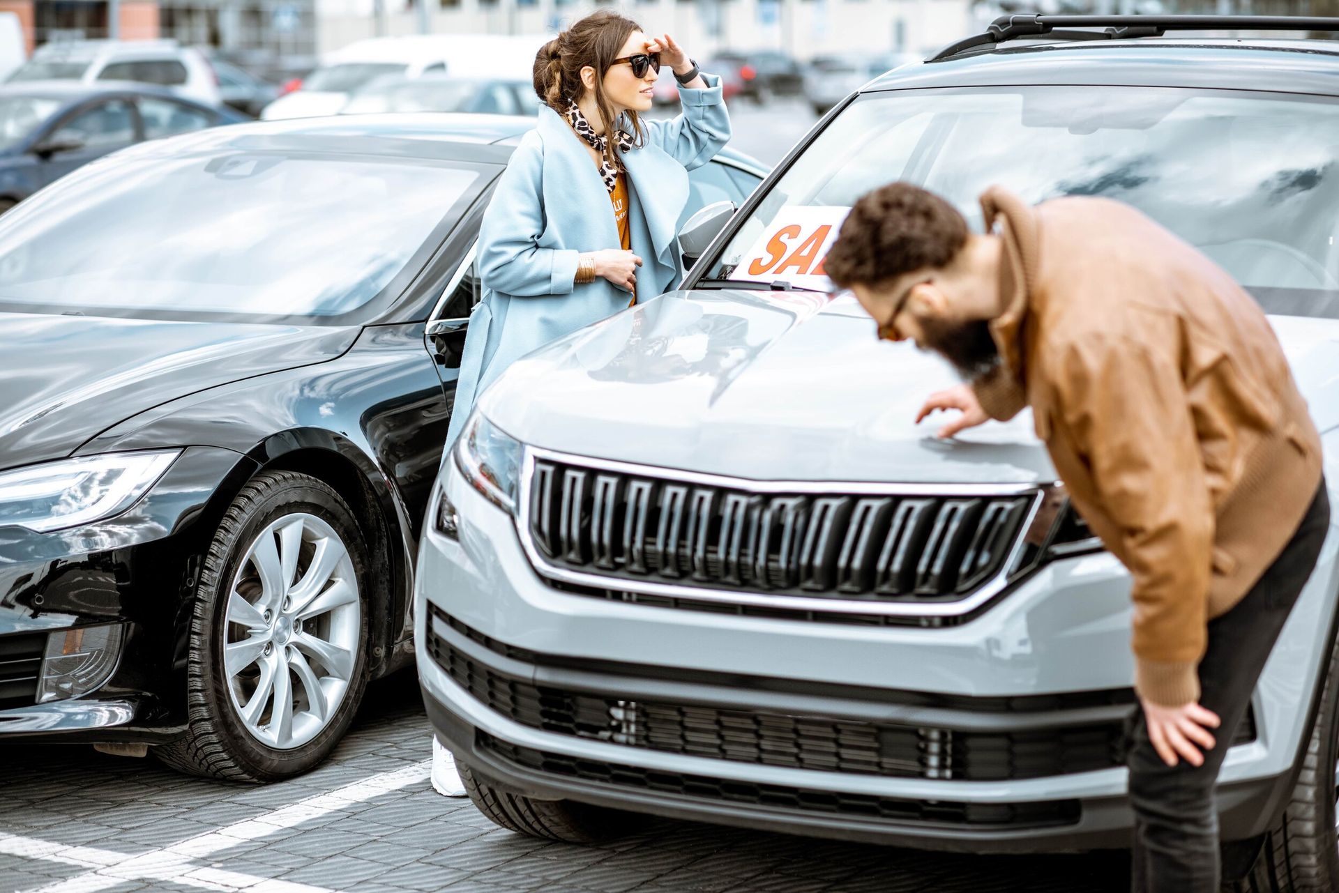 a man and a woman are looking at a car in a parking lot .